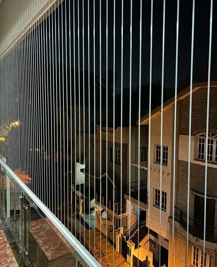 Invisible grill cables across a balcony at night, the street view still clear behind them