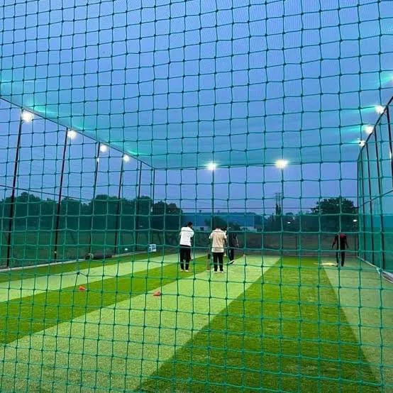 Players practising inside a floodlit cricket net
